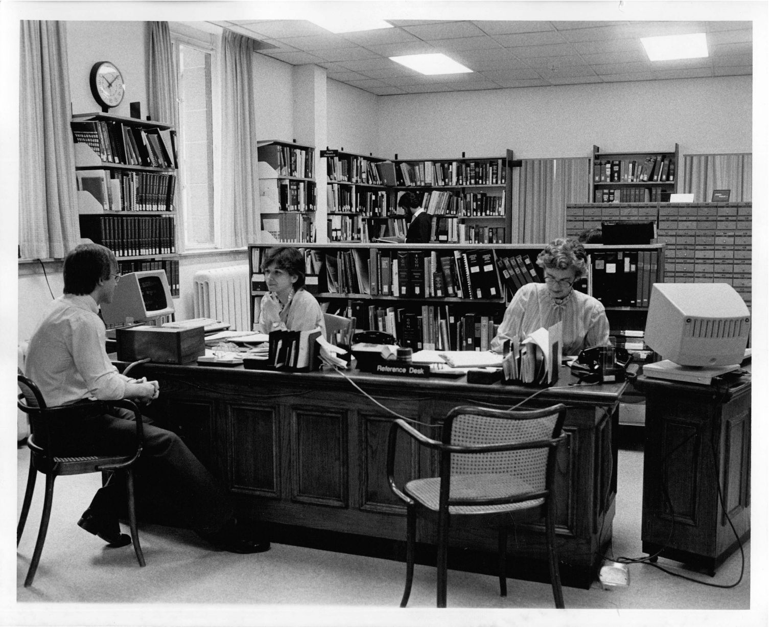 two people seated at one side of the reference desk and one person on the other