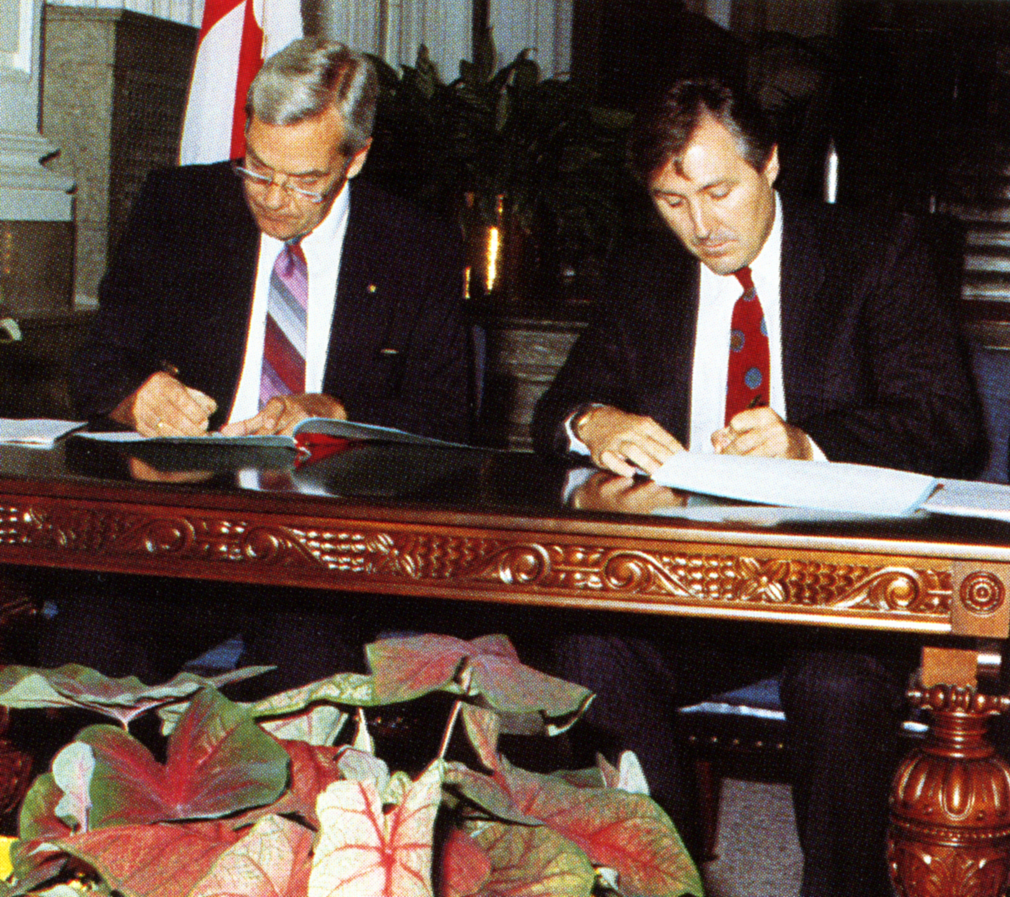 two people seated next to each other at a desk signing papers