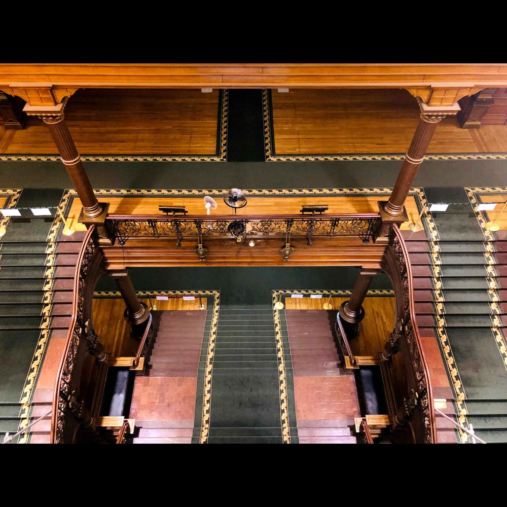 A top down view of the grand staircase showing the two levels, columns, and ironwork.